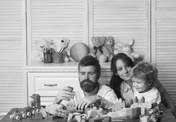 Ojciec, matka i syn w pokoju zabaw na jasnym tle drewnianych. Rodzice i dziecko z skoncentrowane twarze zrobić konstrukcji murowanych. — Zdjęcie stockowe