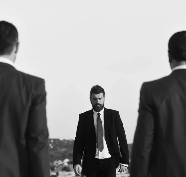 Empresário caminha em direção a dois homens, desfocado. Homem com barba e rosto sério caminha para a frente, de perto . — Fotografia de Stock
