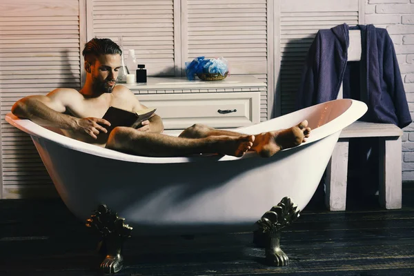 Macho sentado nu na banheira e lendo livro. Sexualidade e conceito de relaxamento: homem com livro de leitura de barba — Fotografia de Stock