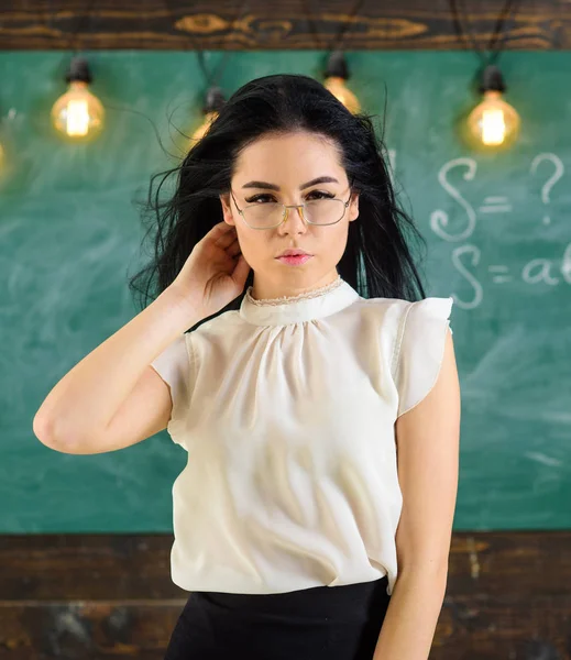 Vrouw met lange haren in witte blouse staat in de klas. De strenge leraar Lady op ontspannen gezicht staat voor schoolbord. Sexy leraar concept. Leraar met glazen en wapperende haren ziet er sexy — Stockfoto