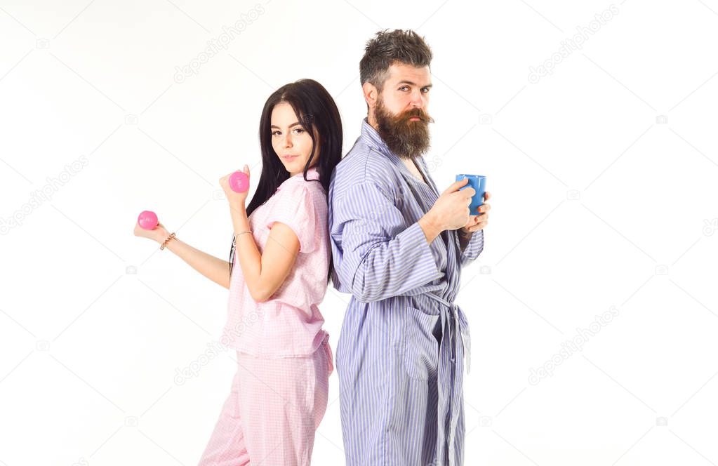 Couple, family on sleepy faces, full of energy. Couple in love in pajama, bathrobe stand isolated on white background. Girl with dumbbell, man with coffee cup. Morning alternative concept