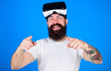 Mavi arka plan üzerinde bulanık Vr bardaklarda uzun sakallı adam. Hippi trendy sakal ve dövme kamera işaret. Adam yeni cihazlar, reklam kavramı teşvik neşeli gülümsemeyle sakallı