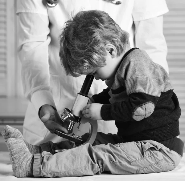 Chico hace experimentos sobre fondo de madera. Hombre y niño con la cara ocupada jugando médico o científico . — Foto de Stock