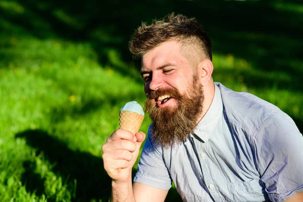 Homem com barba e bigode no rosto feliz come sorvete, grama no fundo, desfocado. Homem com barba longa desfrutar de sorvete, enquanto se senta na grama. Conceito de delicadeza. Homem barbudo com cone de sorvete — Fotografia de Stock