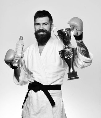 Karate adam boks eldivenleri gülümseme şişe ve altın Galipleri Kupası tutar. Spor ve kazanan ödül kavramı. Kimono içinde sakallı