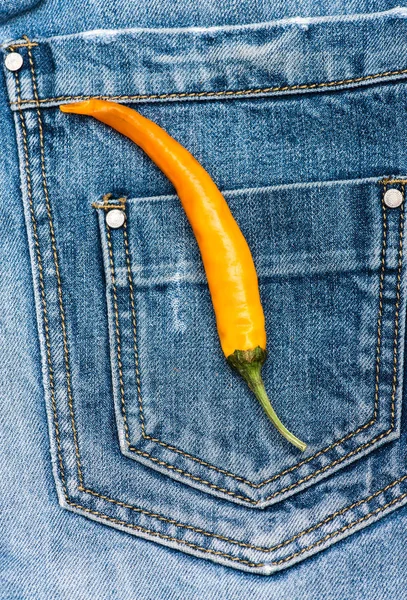 Pocket of jeans with yellow chilly pepper, denim background. Pepper on back pocket of blue jeans. Hot sensations concept. Piquant secret in pocket of pants, top view