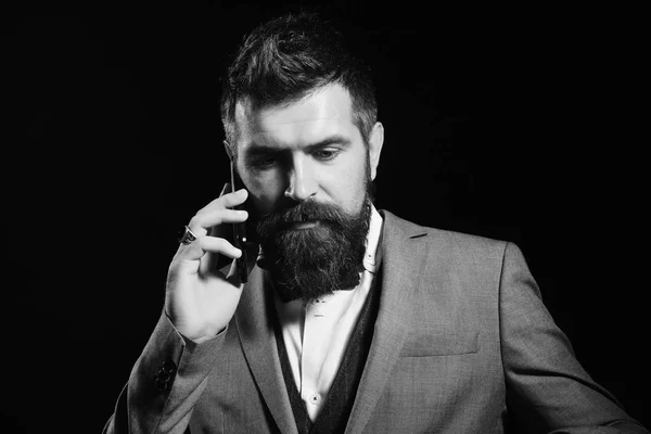 Businessman with busy face isolated on black background. Man with long beard holds mobile phone. Business and phone talk concept. Macho in formal suit — Stock Photo, Image