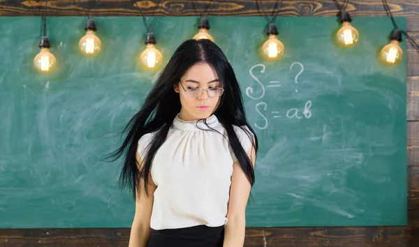 De strenge leraar Lady op kalme gezicht staat voor schoolbord. Vrouw met lange haren in witte blouse staat in de klas. Leraar met glazen en wapperende haren ziet er aantrekkelijk uit. Strenge leraar concept — Stockfoto