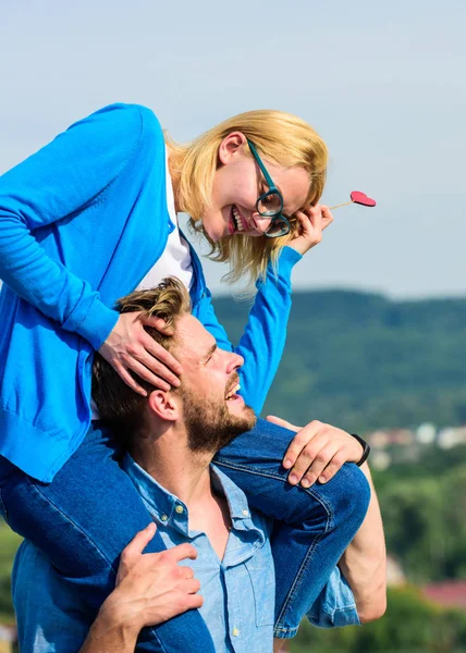 Conceito de data romântica. Homem carrega namorada nos ombros, fundo do céu. Casal apaixonado andando ao ar livre dia ensolarado. Casal feliz encontro se divertindo juntos. Mulher mantém o coração no vara símbolo do amor — Fotografia de Stock