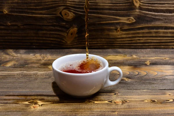 Mug pouring with liquid with splashes and drops of water. Brewing tea concept. Cup pouring with water or tea with splashes on dark wooden background. Cup and teabag on wooden table