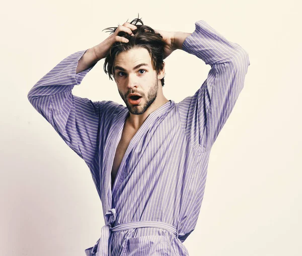 Mañana y concepto de ducha. Hombre con barba en bata azul sobre fondo gris. Macho barbudo en albornoz azul o ropa de ocio. Chico toca el pelo en casa o ropa de baño — Foto de Stock