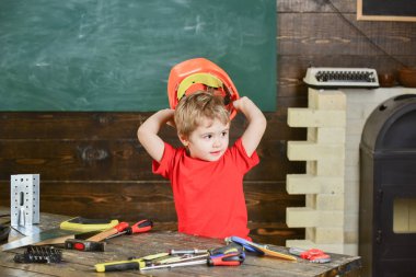 Turuncu koruyucu kask başının üstünde tutan küçük bir çocuk. Çalışma donanımları ile oynayan çocuk. Having oyunculuk atölyesinde preschooler