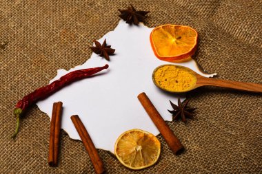 Tarçın, kurutulmuş portakal ve biber, anasonu boş kağıt, tarifi, kopya alanı çevresinde. Mutfak tarifi kavramı. Çul arka plan üzerinde kağıt parçası. Baharat kaşıkla beyaz kağıt yatıyordu