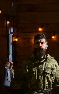 Hakem kavramı. Avcı, av için hazır elinde tabanca ile acımasız hipster. Maço gamekeepers evinde sıkı yüzünde. Sakallı adam ahşap iç arka planda kamuflaj elbiseler giyer