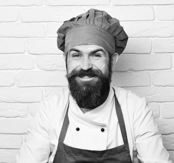 Cuocere con la barba in cappello bordeaux con farina sul viso. Chef con ampio sorriso. Concetto professionale. Uomo dal viso felice — Foto Stock