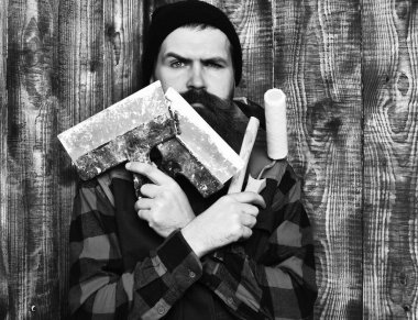 Sakallı inşaatçı ciddi yüzlü çeşitli inşaat aletleri tutuyor.