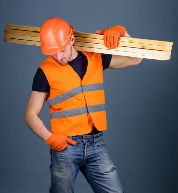 Hardy işçi kavramı. Adam kask, kask ve koruyucu eldiven tutan ahşap kiriş, gri arka plan. Marangoz, woodworker, işçi, meşgul yüz taşıdığı ahşap kirişler omuz üzerinde Oluşturucu