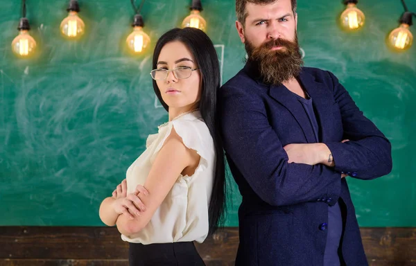 Sakal ve gözlük stand sırt sırta, kara tahta arka plan öğretmen olan adam. Öğretmen ve öğretmen rahat görünüyor. Okul personeli kavramı. Bayan ve birlikte okulda çalışan hipster