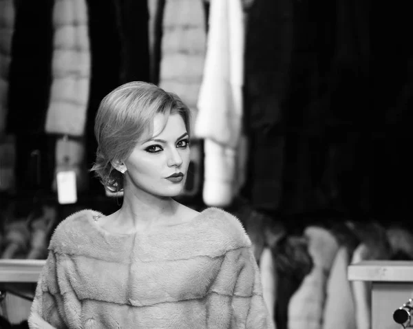 Frau mit blonden Haaren kauft pelzigen Mantel. Dame probiert teuren grauen Nerzmantel an. Reiches Modekonzept. — Stockfoto