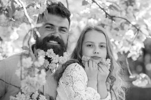 Niño y hombre con tiernas flores rosas en barba. Concepto de infancia. Padre e hija en caras felices juegan con flores, fondo de sakura. Chica con papá cerca de flores de sakura en el día de primavera — Foto de Stock