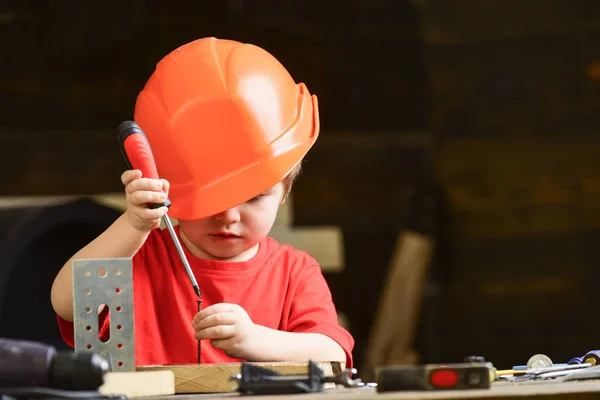Jungen spielen als Bauarbeiter oder Reparateur, arbeiten mit Werkzeugen. Kind, das von einer Karriere in der Architektur oder im Bauwesen träumt. Kindheitskonzept. Junge mit orangefarbener Mütze oder Helm, Hintergrund im Arbeitszimmer — Stockfoto