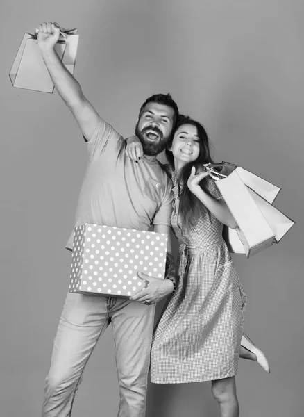 Couple in love holds shopping bags on yellow background. Man with beard holds red polka dotted box