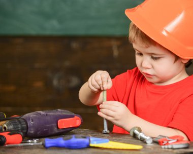 Yürümeye başlayan çocuk meşgul yüzündeki evde atölyede civata ile oynuyor. Kavram handcrafting. Baret, Oluşturucusu'nu veya repairer, handcrafting onaltılık cıvata ile oynarken kask çocuk. Çocuk Çocuk tamirci oynamak