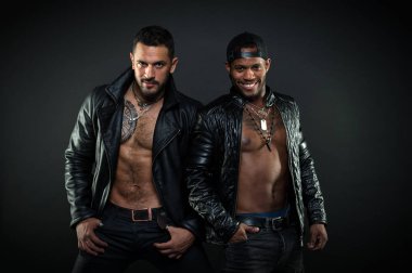 Deri erkek giyim kavramı. Seksi kas torsolar erkeklerle vahşice bak. Erkekler gülümseyen yüzler kıl ile üzerinde. Maço kas torsolar ile deri ceketler, koyu arka plan çekici bakmak