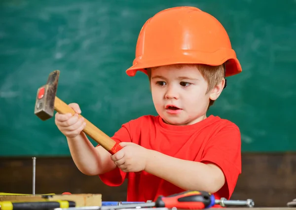 Miúdo excitado a brincar com martelo pesado. Rapaz bonito em capacete laranja ajudando na oficina. Conceito de profissão futura — Fotografia de Stock