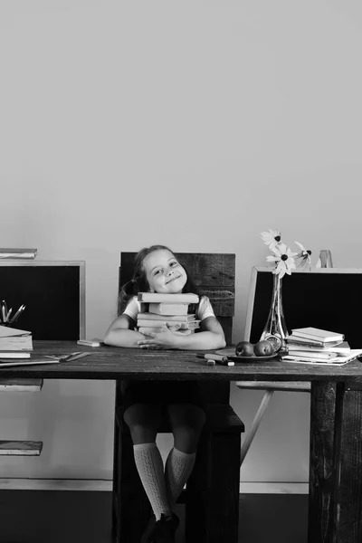 Детство и возвращение к школьной концепции. Девушка сидит за столом с красочными канцелярскими принадлежностями, цветами и фруктами — стоковое фото