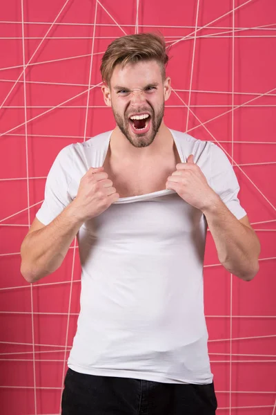 Chico barbudo atractivo arrancando la camisa. Concepto masculinidad. El hombre con barba sin afeitar se ve guapo y bien arreglado. Hombre con cerdas gritando cara agresiva desvestirse, fondo rosa — Foto de Stock