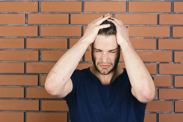 Um tipo com uma ligeira cerda de tshirt azul escura, segura as mãos na cabeça. Macho exausto por sofrer de dor de cabeça. Linguagem corporal e conceito de saúde. Homem com cabelo claro — Fotografia de Stock