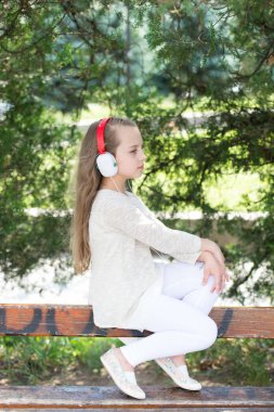 Moda çocuk ve modern teknoloji. Yaz Park müzik dinle küçük kız. Çocuk müzik kulaklık açık keyfini çıkarın. Melodi ses ve mp3. Yaz tatili ve eğlenceli