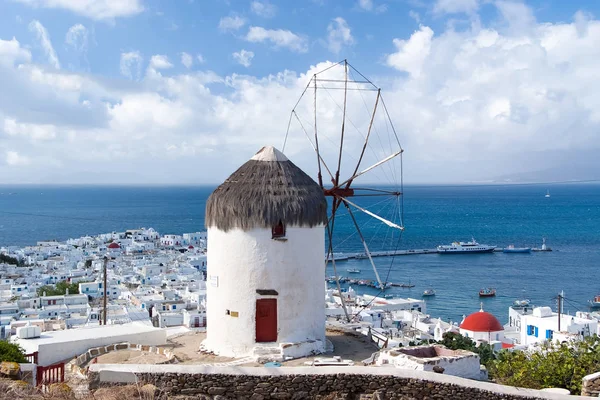 Windmill on mountain by sea in Mykonos, Greece. Windmill on seascape on cloudy sky. White building with sail and straw roof with nice architecture. Summer vacation on island. Landmark and attraction