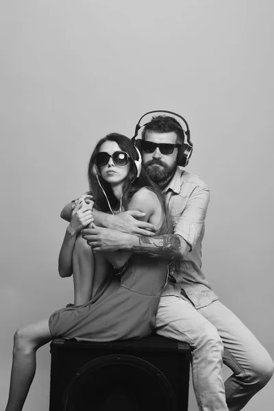 Verliefde paar zit op luidspreker op roze achtergrond. Man met baard draagt hoofdtelefoons en zonnebril. — Stockfoto