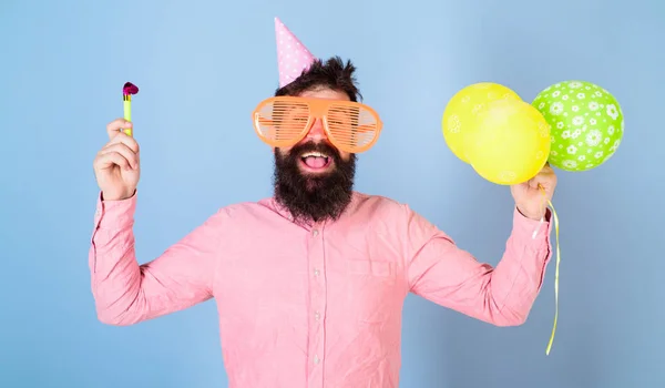 Hombre con barba y bigote en la cara feliz sostiene globos de aire, fondo azul claro. Hipster en vasos gigantes celebrando su cumpleaños. El tipo con sombrero de fiesta con atributos navideños celebra. Concepto del partido —  Fotos de Stock