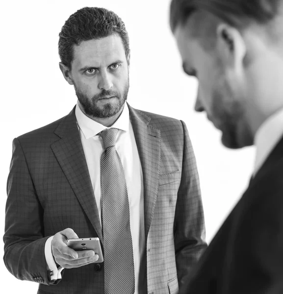 Business and technologies concept. Businessmen checking economic markers on gadgets. Men in classic suit or businessmen with strict face hold smartphone on white background.