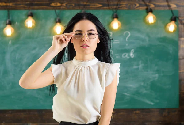 Vrouw met lange haren in witte blouse staat in de klas. Strenge leraar concept. De strenge leraar Lady op kalme gezicht staat voor schoolbord. — Stockfoto
