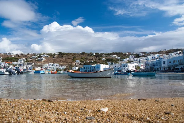 Fishing boats on sea beach in Mykonos, Greece. Sea village on cloudy sky. White houses on mountain landscape with nice architecture. Summer vacation on mediterranean island. Wanderlust and travelling