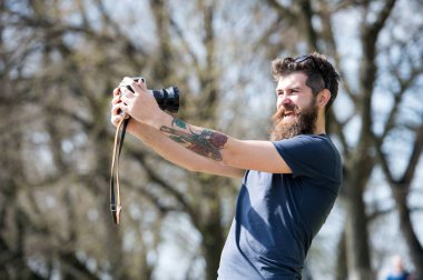 Sakallı adam selfie vintage kameraya alıyor. Sakal ve bıyık neşeli yüzündeki defocused arka plan, dallarda olan adam. Selfie alarak meşgul uzun sakallı adam. Fotoğrafçı kavramı
