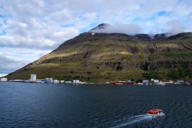 İzlanda gezisi. Sejdisfjordur, İzlanda dağ manzarası denizde tekne float. Bulutlu gökyüzü dağda ile yalı. Su ile seyahat. Macera ve keşif. Yaz tatil ve yolculuk tutkusu