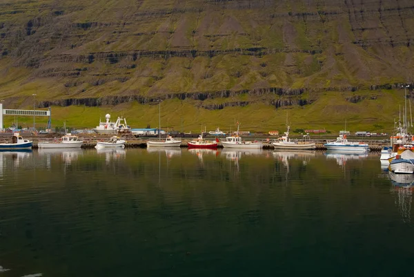 Boats docked in sea on mountain landscape in Sejdisfjordur, Iceland. Water crafts at sea coast. Travelling by water. Adventure and discovery. Summer vacation and wanderlust