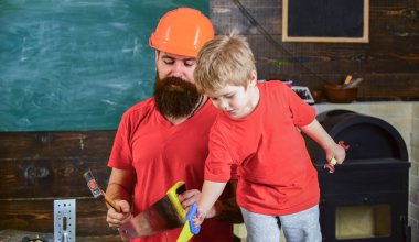 Evlat, çocuk oyuncakla oynamak neşeli, öğrenme kullanım araçları babamla gördüm. Baba, üst koruyucu kask okul atölyesinde farklı araçları kullanmak için küçük oğlu öğretim içinde sakallı. Babalık kavramı