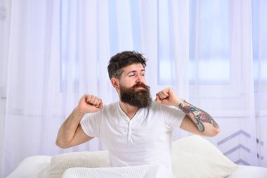 Adam silah, sabah enerji dolu germe. Mükemmel sabah kavramı. Nap sonra rahatlatıcı maço memnun yüz germe üzerinde bekletin. Tişörtlü adam yatak, beyaz perde arka plan üzerinde oturur