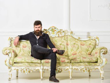Hipster sıkı yüzünde yalnız oturuyor. Zengin ve yalnız kavramı. Sakallı ve bıyıklı lüks oturma odasında boş zaman harcıyor. Lüks daire sahibi beyaz duvar arka koltukta oturur