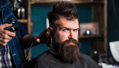 Berberler saç kesme makinesi kırpma ile ver. Şık saç kesimi kavramı. Eller berberin kesme makinesi ile kapatın. İstemci salon zemin üzerine sakallı. Hipster sakallı istemci üzerinde katı yüz saç modeli elde