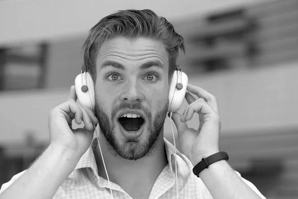 Music and sound concept. Man with unshaven face enjoy sound with modern headphones. Macho with surprised face likes music. Young man listening music