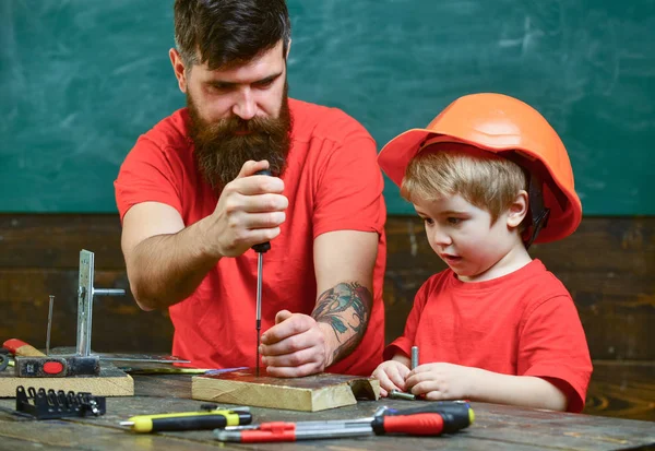 Fiú, gyermek elfoglalt védő sisak, a tanulás csavarhúzóval, apa. Javítási és workshop koncepció. Apja, szülő szakáll oktatási eszköz csavarhúzóval kis fia — Stock Fotó