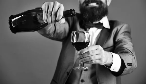 Copo e garrafa de vinho tinto em foco seletivo. Homem com barba no fundo vermelho derrama vinho italiano — Fotografia de Stock