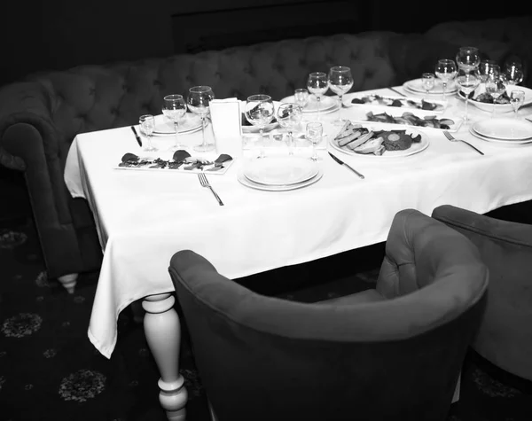 Tavolo con panno bianco vicino poltrone rosse e divano. Tavola ristorante servita con snack e insalate . — Foto Stock